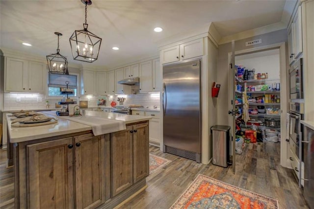 kitchen featuring built in appliances, a center island, hardwood / wood-style floors, white cabinets, and pendant lighting