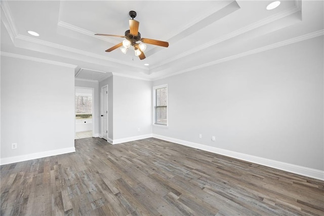 empty room with attic access, a raised ceiling, baseboards, and wood finished floors