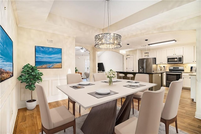 dining room featuring a raised ceiling, light hardwood / wood-style flooring, ceiling fan, and ornamental molding