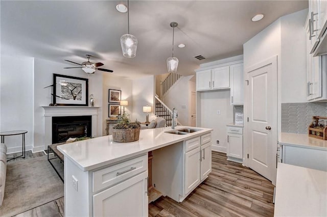 kitchen featuring light wood finished floors, open floor plan, a kitchen island with sink, white cabinetry, and a sink