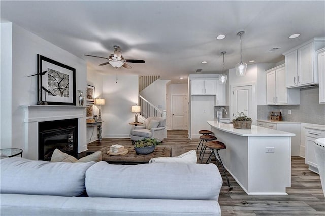 living area featuring recessed lighting, wood finished floors, baseboards, stairway, and a glass covered fireplace