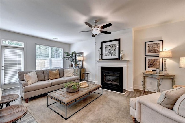 living area featuring baseboards, wood finished floors, a ceiling fan, and a glass covered fireplace