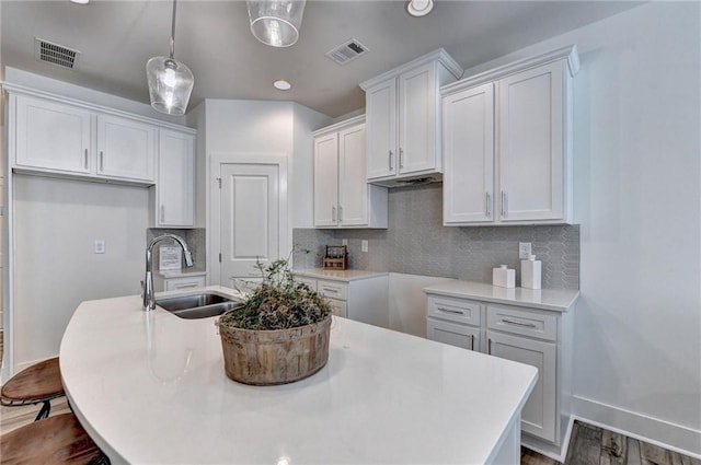 kitchen featuring a kitchen island with sink, visible vents, a sink, and white cabinetry