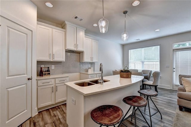 kitchen featuring visible vents, light wood-style flooring, a sink, white cabinetry, and backsplash