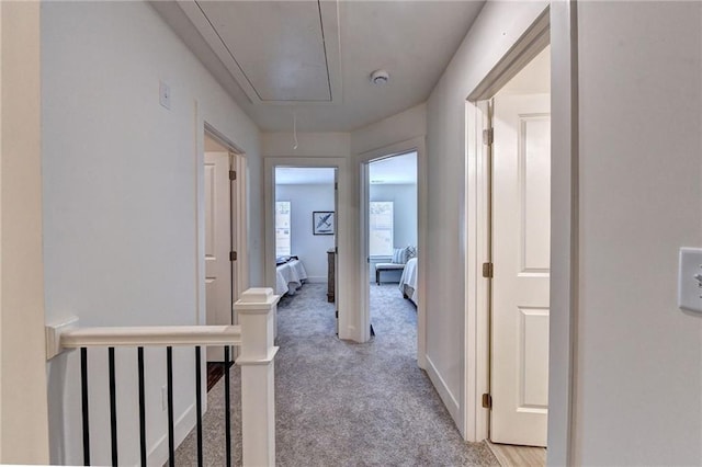 hall with light carpet, attic access, and baseboards