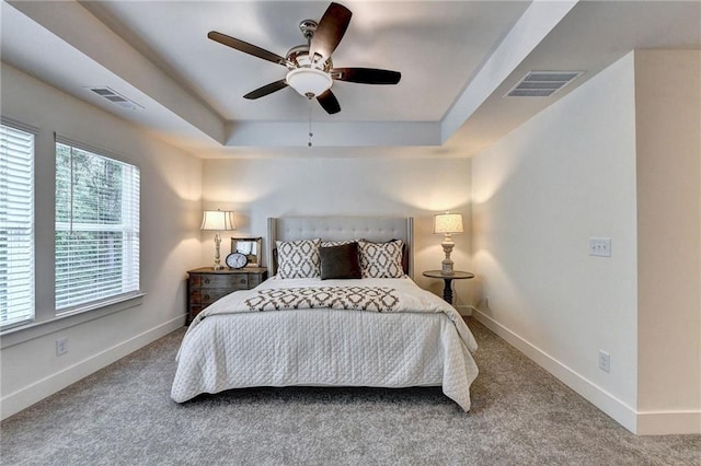 bedroom featuring carpet floors, a tray ceiling, visible vents, and baseboards