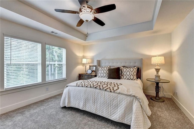 carpeted bedroom featuring a ceiling fan, a raised ceiling, visible vents, and baseboards