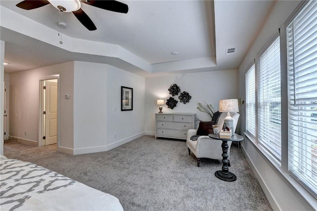 carpeted bedroom with a ceiling fan, visible vents, a tray ceiling, and baseboards