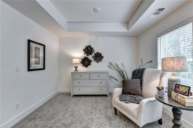 living area featuring light colored carpet, a tray ceiling, visible vents, and baseboards