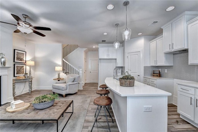 kitchen with a kitchen island with sink, light wood-style flooring, white cabinetry, visible vents, and tasteful backsplash