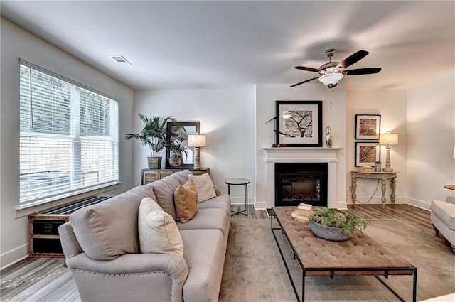 living area with a healthy amount of sunlight, visible vents, wood finished floors, and a glass covered fireplace