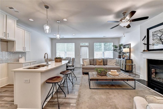 living area featuring baseboards, a glass covered fireplace, visible vents, and light wood-style floors