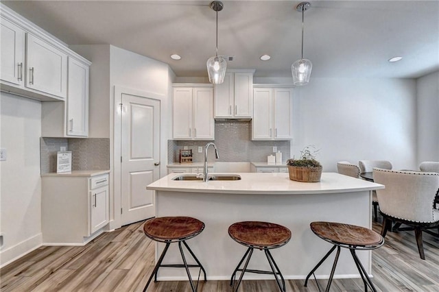 kitchen with a breakfast bar, decorative light fixtures, light wood-style flooring, white cabinetry, and a sink