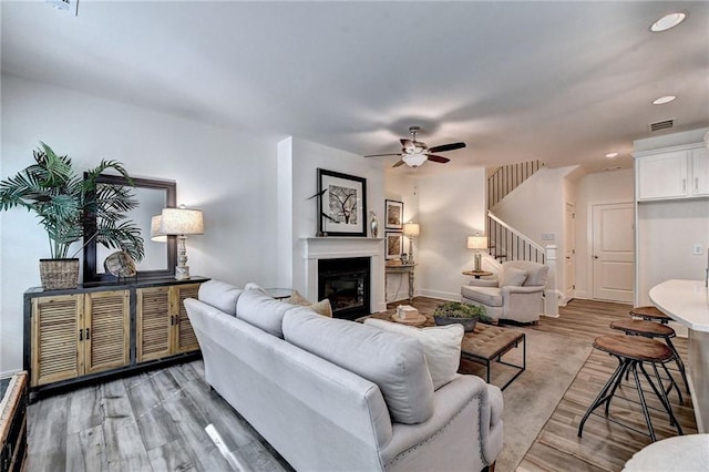 living room with baseboards, a ceiling fan, a glass covered fireplace, stairway, and light wood-style floors