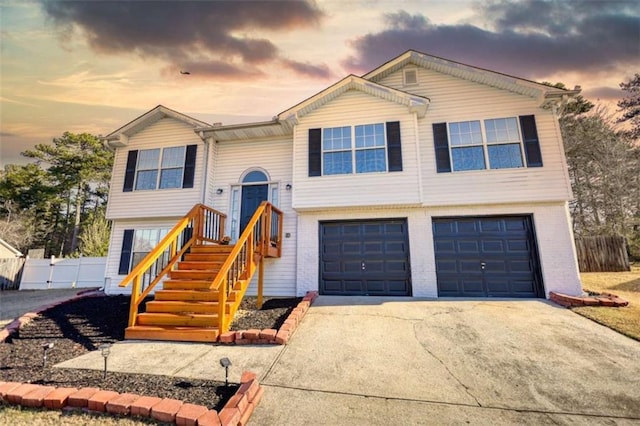 bi-level home featuring a garage, brick siding, concrete driveway, and fence