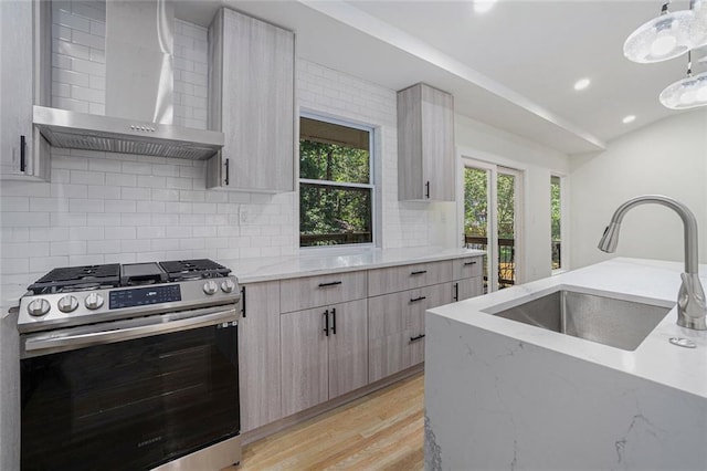 kitchen featuring a sink, light stone counters, stainless steel range with gas cooktop, wall chimney exhaust hood, and light wood finished floors