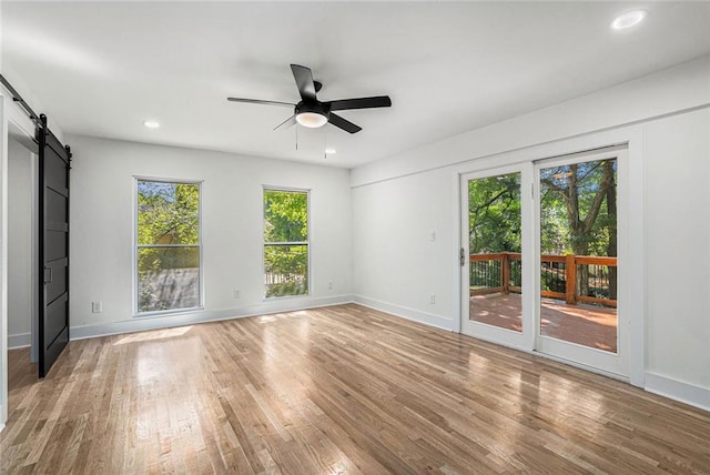 empty room with a barn door, baseboards, light wood-type flooring, and ceiling fan