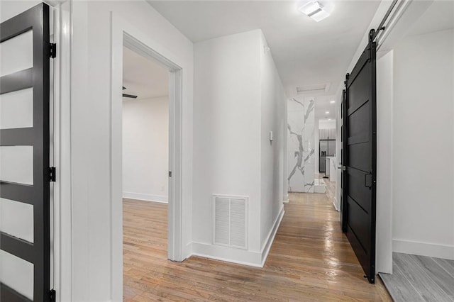 hallway featuring visible vents, baseboards, light wood-type flooring, and a barn door