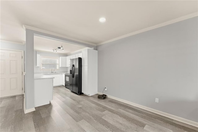 kitchen featuring sink, white cabinets, crown molding, black fridge, and light wood-type flooring