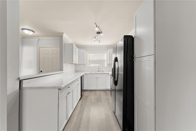 kitchen with sink, white cabinets, backsplash, light hardwood / wood-style floors, and black fridge