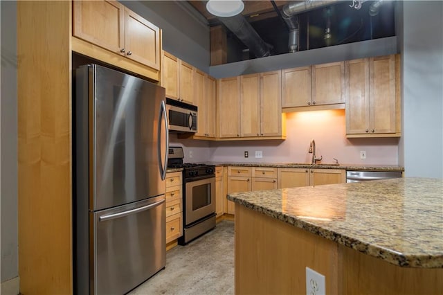 kitchen with light brown cabinetry, stainless steel appliances, light stone counters, and a sink