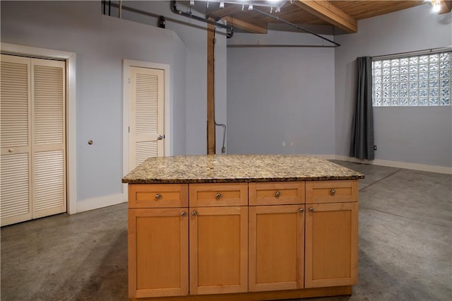 kitchen with light stone counters, baseboards, beam ceiling, and finished concrete flooring