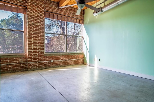 empty room featuring a wealth of natural light, brick wall, concrete floors, and baseboards