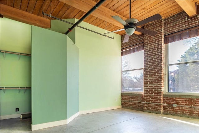 unfurnished room with beamed ceiling, baseboards, concrete flooring, and brick wall