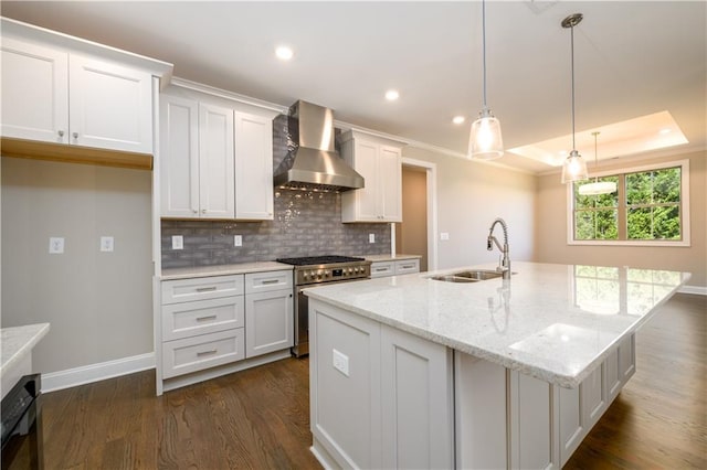 kitchen with hanging light fixtures, white cabinets, sink, wall chimney range hood, and stainless steel range