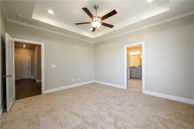 unfurnished bedroom with connected bathroom, a tray ceiling, ceiling fan, ornamental molding, and light carpet