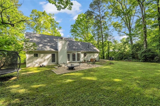 back of property with a chimney, a trampoline, an outdoor fire pit, a yard, and a patio
