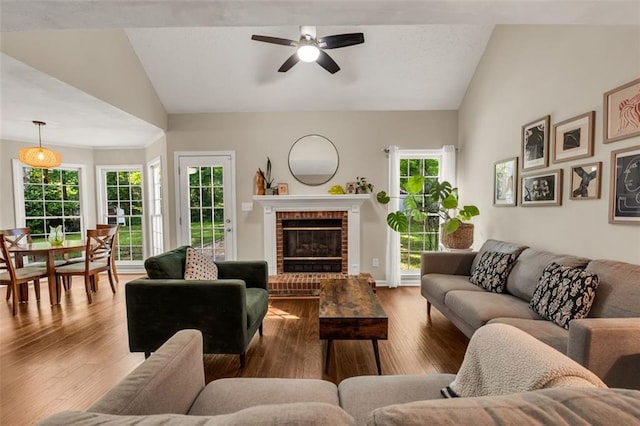 living area featuring a fireplace, a ceiling fan, vaulted ceiling, and wood finished floors