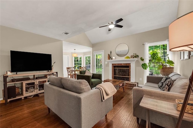 living area with visible vents, a fireplace, a ceiling fan, dark wood finished floors, and vaulted ceiling