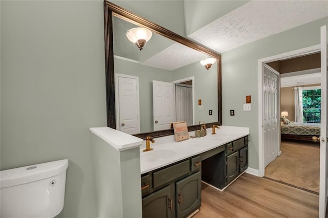 bathroom featuring double vanity, wood finished floors, toilet, a sink, and ensuite bath