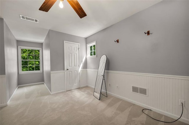 unfurnished bedroom featuring carpet floors, a wainscoted wall, a ceiling fan, and visible vents