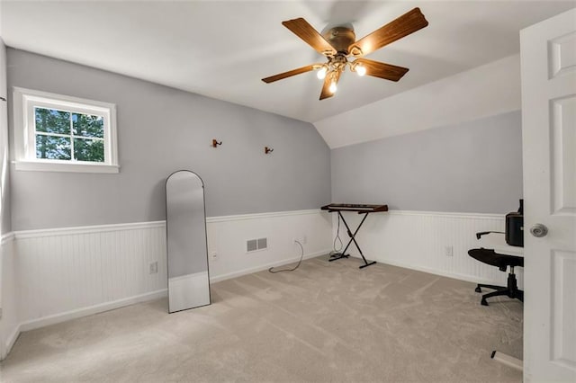 unfurnished office featuring visible vents, carpet floors, wainscoting, lofted ceiling, and a ceiling fan