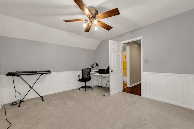 carpeted home office with ceiling fan, wainscoting, and lofted ceiling
