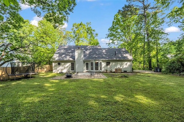 rear view of house with a trampoline, a patio area, fence, an outdoor fire pit, and a yard
