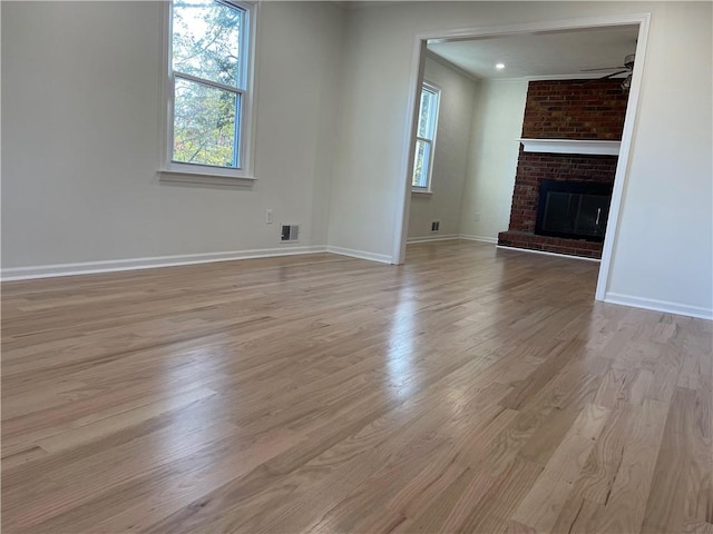 unfurnished living room with a brick fireplace, ceiling fan, ornamental molding, and light wood-type flooring