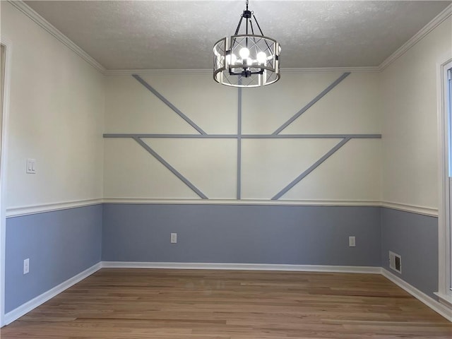 unfurnished dining area featuring a notable chandelier, wood-type flooring, a textured ceiling, and ornamental molding