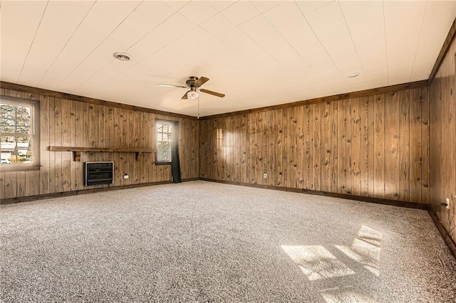 unfurnished living room with heating unit, carpet floors, wood walls, baseboards, and ceiling fan