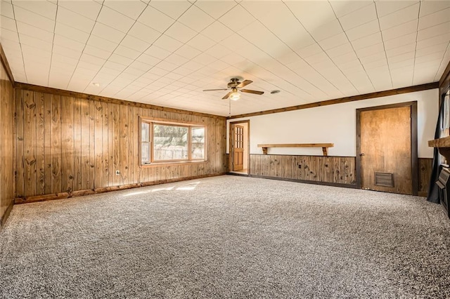 carpeted spare room featuring visible vents, wooden walls, and ceiling fan