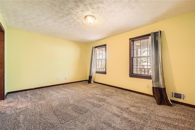 unfurnished room with baseboards, visible vents, carpet floors, and a textured ceiling