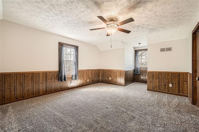 carpeted spare room with visible vents, wood walls, wainscoting, and vaulted ceiling