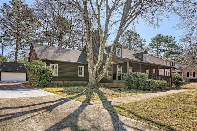 view of front of house featuring an outbuilding, roof with shingles, covered porch, a chimney, and a garage