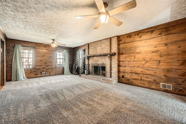 unfurnished living room with wooden walls, carpet flooring, a fireplace, and visible vents