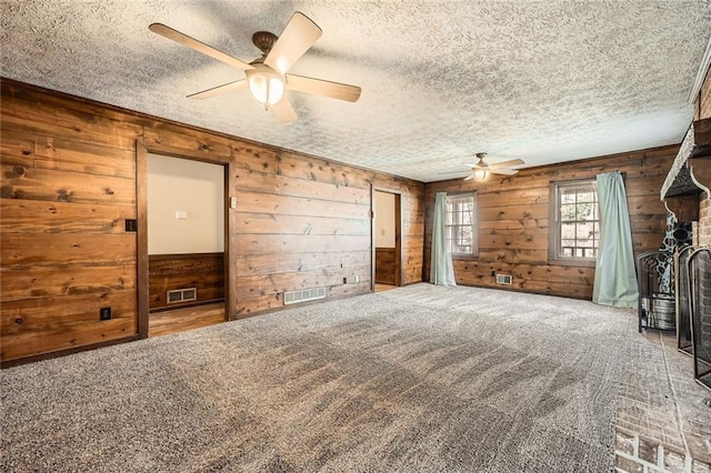 carpeted empty room featuring visible vents, a textured ceiling, and wooden walls