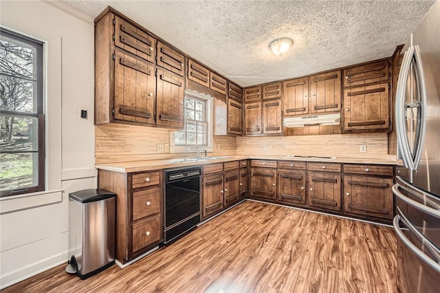 kitchen featuring under cabinet range hood, black dishwasher, freestanding refrigerator, light wood-style floors, and light countertops