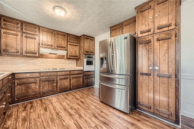 kitchen with under cabinet range hood, appliances with stainless steel finishes, light countertops, and wood finished floors