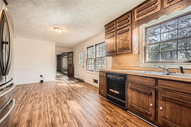 kitchen with a sink, black dishwasher, wood finished floors, freestanding refrigerator, and light countertops